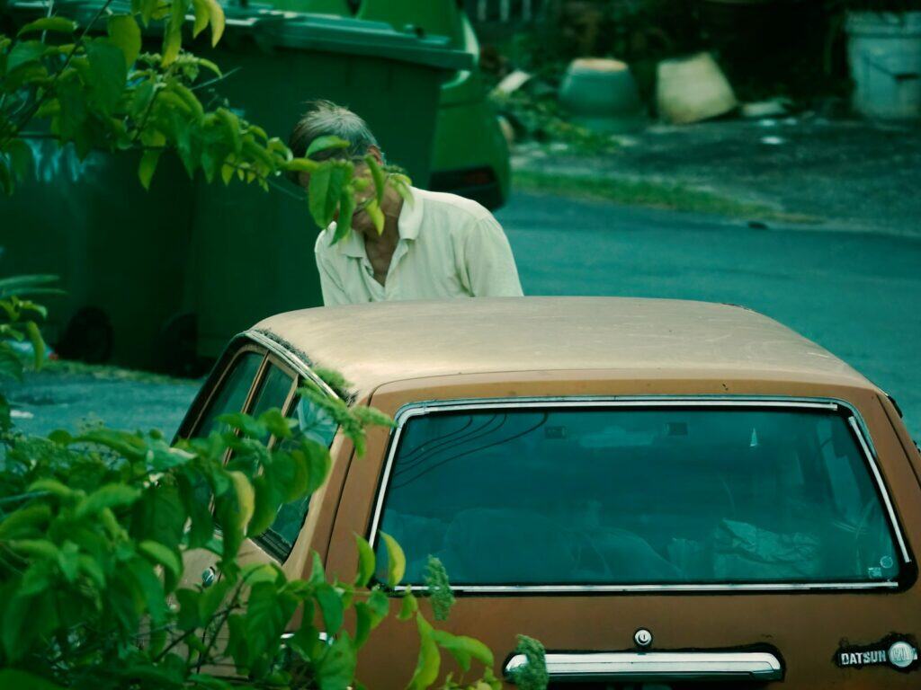 Man bending over an old car near bins